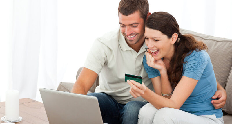 Happy couple looking at their accounts online sitting on the sofa at home